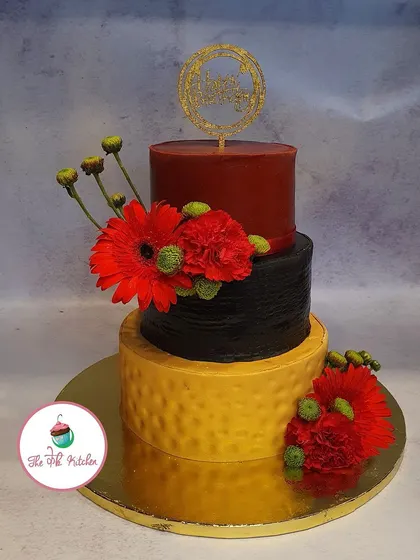 A bold and modern three-tiered cake with strong color blocking in red, black, and yellow. The textured bottom tier and fresh red gerberas create a striking look.