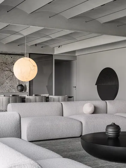The formal living room of the Vaulted Haus showcases a refined grey scale material palette. The texture of the bouclé sofa, the smooth black coffee table, and the vaulted ceiling create a rich, monochromatic scheme.