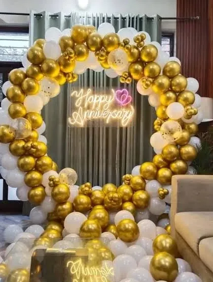 A luxurious anniversary setup in a living room, featuring a full circular balloon arch in gold and white with a neon sign.