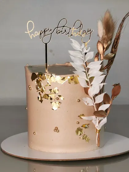 This simple yet elegant birthday cake features a neutral-toned buttercream, edible gold leaf, and a spray of dried, painted leaves for a modern and rustic feel.