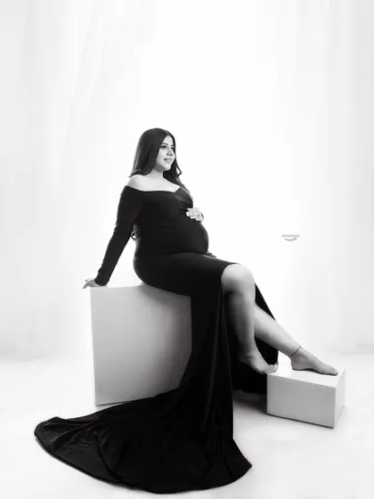 A classic black and white studio portrait. The client is seated in an elegant black gown against a bright, clean background, creating a timeless and sophisticated look.