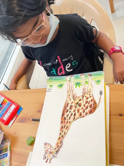 A student concentrating on her color pencil drawing of a giraffe. It takes focus to get all those spots and the gentle expression just right.