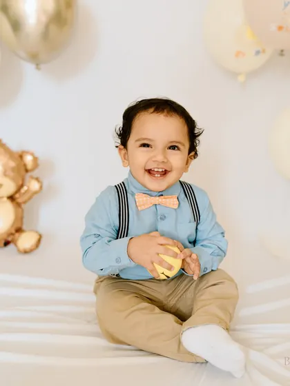 Dressed up and ready to party! This little gentleman's first birthday portrait is full of smiles, with a classic setup of balloons and a teddy bear.