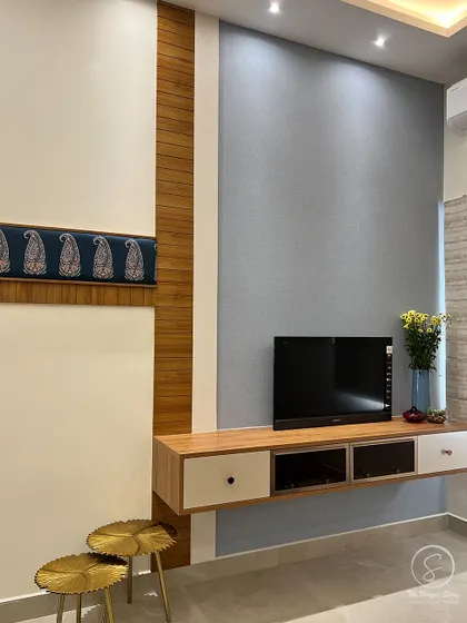 A floating TV unit in the bedroom, designed with a mix of wood and white finishes. The wall is treated with two different textures and a paisley fabric accent, echoing the room's Indian contemporary theme.