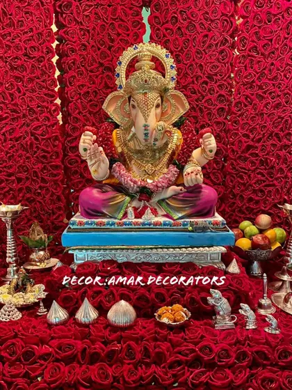 A close up of the Ganpati idol against the rich red rose backdrop. The silver puja accessories and modaks stand out beautifully against the vibrant color.