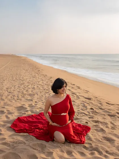 A wide shot showing the beautiful expanse of the beach and the mom-to-be in her element. The red gown provides a stunning pop of color against the neutral sand and sea.