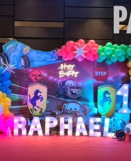 A high-energy Disney Cars theme for Raphael's first birthday. The setup includes character cutouts of Lightning McQueen and Mater, a racetrack-inspired backdrop, and marquee letters spelling out the name.