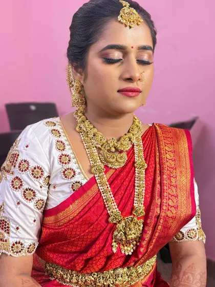 A classic muhurtham look with a red and white silk saree. The makeup features a bold red lip and defined eyes, perfect for a traditional ceremony.