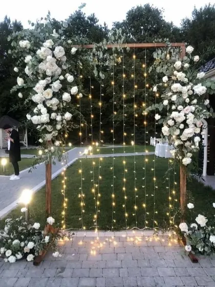 This photo booth design is perfect for an elegant evening event. A simple wooden arch is adorned with lush white roses and greenery, with a curtain of twinkling fairy lights in the center that creates a romantic and dreamy atmosphere.