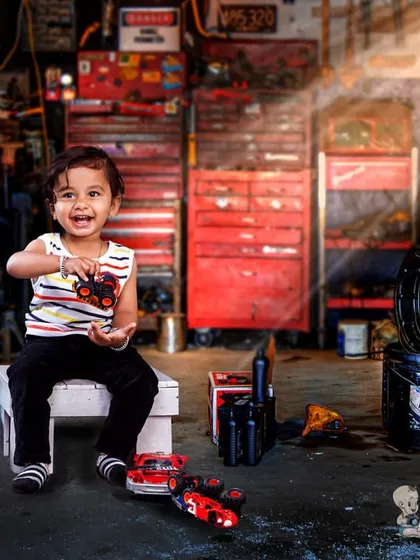 A happy toddler having fun in a realistic garage setup, complete with tool chests and a stop sign. His joyful expression shows just how much fun these imaginative shoots can be.