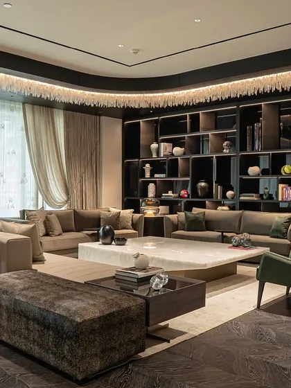 This grand living room at DLF Camellias is defined by its custom shelving and dramatic lighting. The space is furnished with multiple seating groups, including a large sofa and comfortable armchairs, creating a versatile environment for both large gatherings and quiet moments.