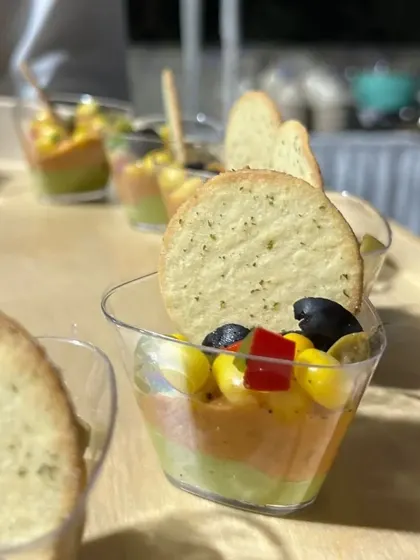 This layered dip cup features guacamole, salsa, and a creamy base, served with a crisp cracker. It's a deconstructed and refined take on a classic favorite, perfect for individual servings.