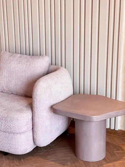 A detail shot showing the texture of a lilac bouclé armchair next to a matching side table with a smooth, micro-topped concrete finish. This highlights our love for combining different tactile materials.