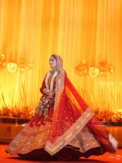 A stunning full-length shot of the bride, her red and gold lehenga catching the light beautifully. Her twirl shows off the magnificent flare of her dress, making her look like a queen.
