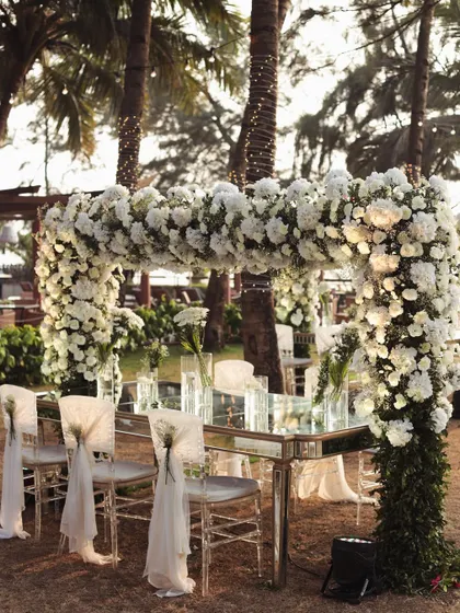 A stunning floral arch frames the dining setup for a beach wedding, allowing guests to dine with an uninterrupted view of the ocean.