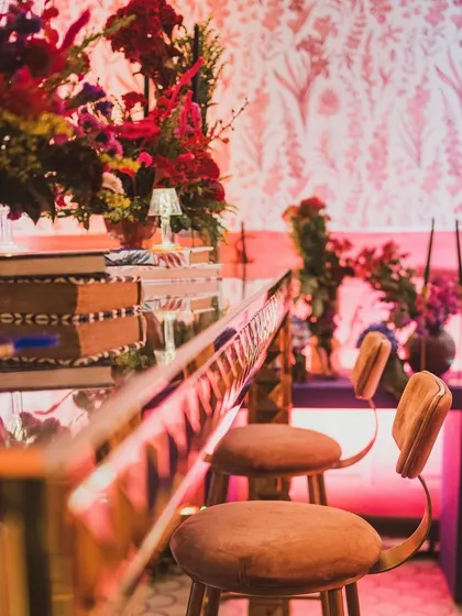 A detail shot of the mirrored bar top reflecting the rich textures of the velvet stools and the intricate floral arrangements.
