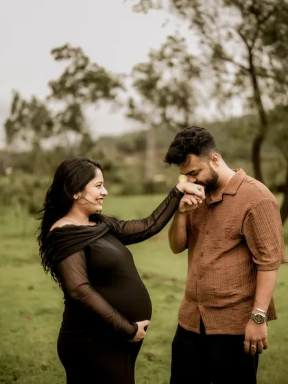 A classic romantic gesture. He gently kisses her hand as she smiles at him, a timeless expression of love and chivalry in a beautiful outdoor setting.
