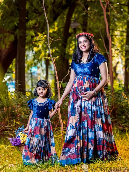A mother and daughter in matching dresses during a maternity photoshoot in the woods. This beautiful outdoor portrait captures the special connection they share as they await the new family member.