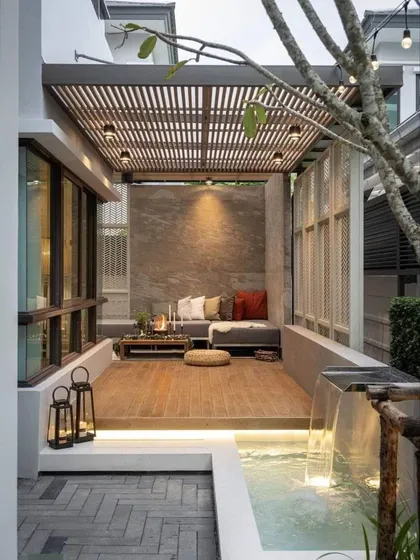 A stunning example of indoor-outdoor living, this patio features a slatted wood pergola and a gentle waterfall that flows into a small pool. The combination of wood, stone, and water creates a serene and natural environment.
