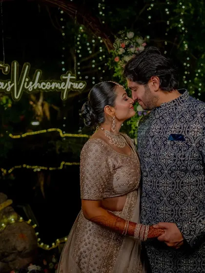 The couple under a neon sign that reads 'TejasVishcometrue', a fun and personalized touch for their reception.