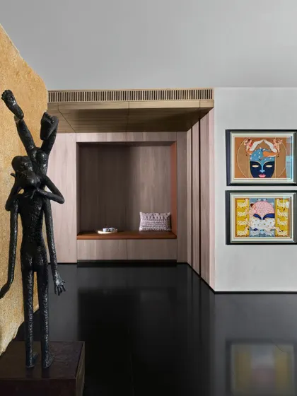 A captivating sculpture by S. Radhakrishnan stands against a stone wall by Odyssey. The dynamic, fluid form of the bronze sculpture contrasts with the solid, textured backdrop, creating a focal point rich in movement and material honesty.