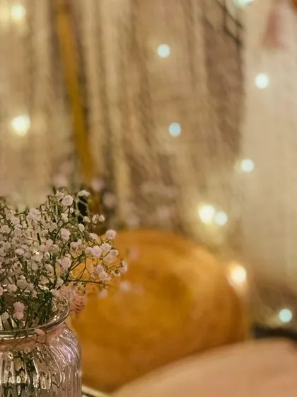 A close-up detail of a romantic setup, showing baby's breath flowers in a glass jar against a backdrop of twinkling fairy lights. It's these small touches that create the magic.