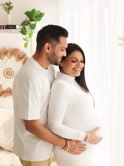 A classic and elegant pose by the window. The expecting couple is bathed in soft, natural light, highlighting the baby bump and their peaceful connection.