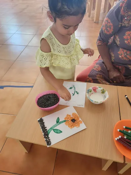 A child carefully works on a seed collage. This activity requires precision and focus, helping to develop the fine motor skills needed for writing.