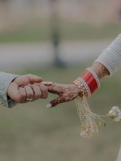 A close up shot of the couple holding hands, focusing on the bride's red chooda and intricate henna design.