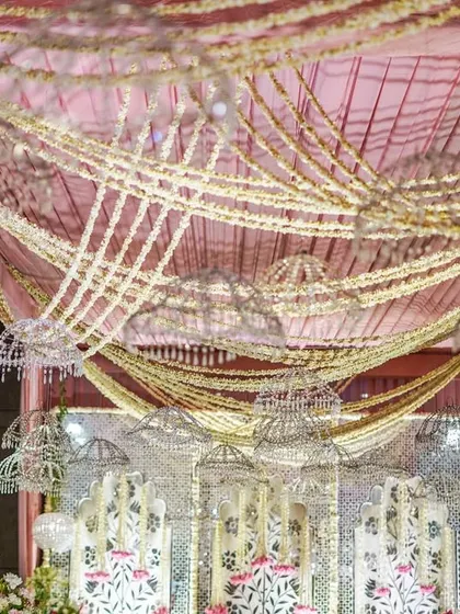 A view of the stage from below, looking up at the intricate ceiling treatment. Garlands of pearls and flowers are draped across a pink fabric canopy, with crystal umbrellas adding sparkle.