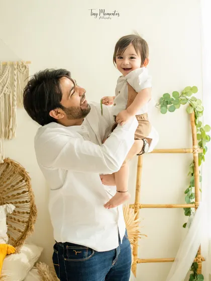 A father's proud and loving gaze as he holds his son. The natural light from the side illuminates their happy faces, creating a warm and uplifting portrait.