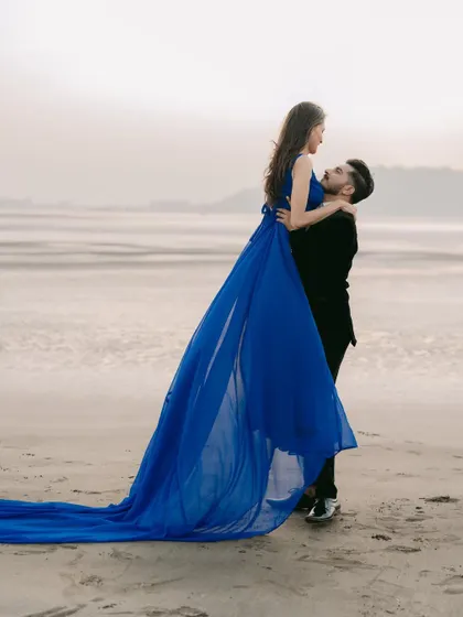 A dreamy lift on the beach. The deep blue trail gown flows behind them, adding a sense of motion and romance to this classic pre-wedding pose.