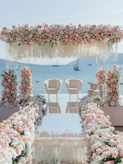 A frontal view of the seaside mandap in Turkey, with a mirrored aisle reflecting the sky and sea. The transparent pillars filled with flowers create an illusion of floating florals, a bespoke design element that enhances the natural beauty of the location.