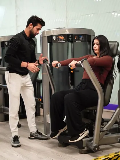 A trainer provides guidance on the pec deck machine, helping a client target her chest muscles correctly and maintain proper form throughout the set.