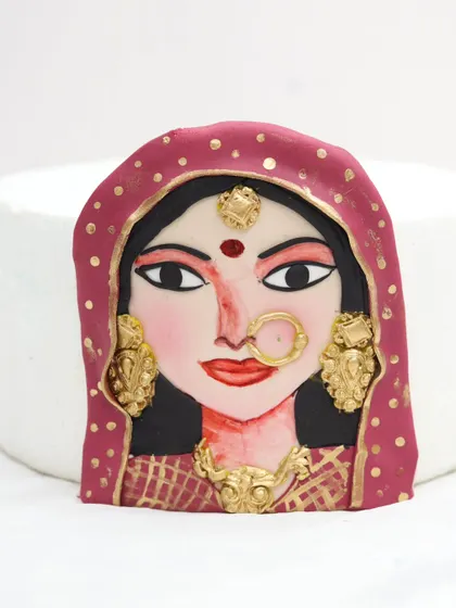A close-up of a hand-painted fondant plaque featuring a traditional Indian bride. This is an advanced technique where students learn to paint intricate details to create a portrait effect.