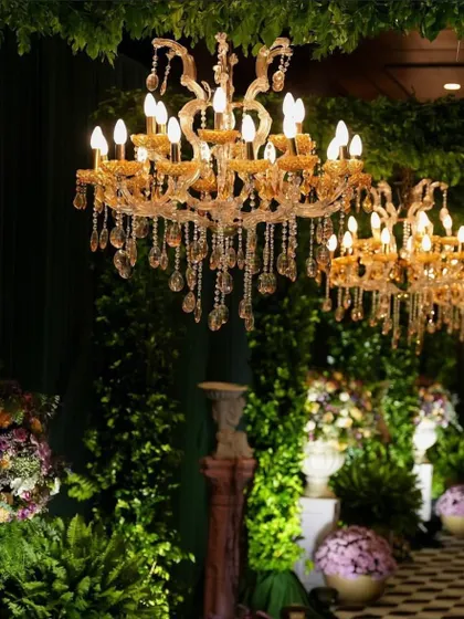 Lighting is key to creating mood. Here, grand crystal chandeliers illuminate a lush green backdrop, adding a touch of classic elegance and warmth to the event space.