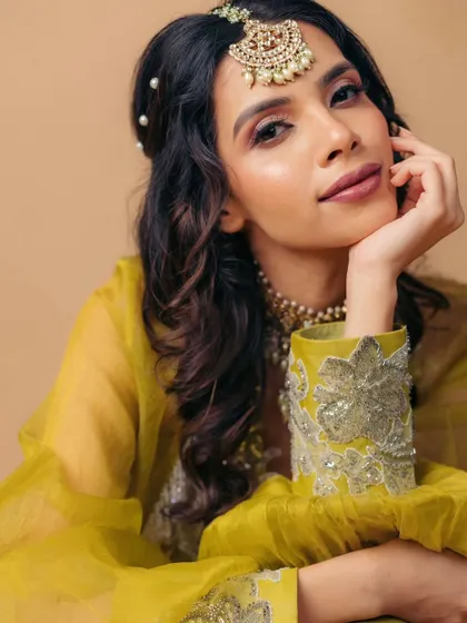 A relaxed and elegant pose. The soft curls, pearl hair accessories, and shimmery makeup create a look that is perfect for a sophisticated mehendi party.