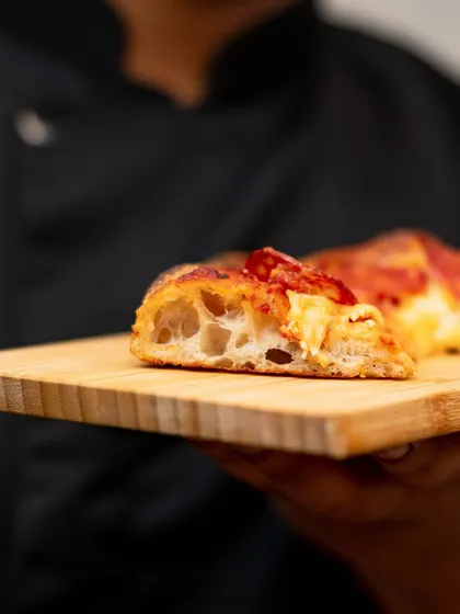 A close-up of the "cornicione," the puffy, airy crust of our Pizza Romana. The open, bubbly structure is a sign of a long, slow fermentation.