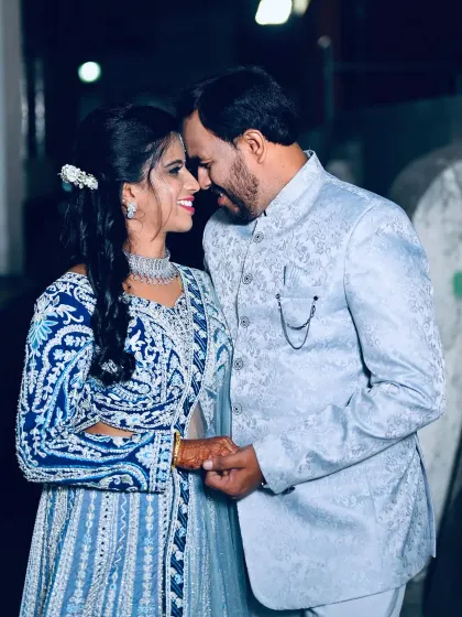 This couple looks perfectly coordinated for their reception or pre-wedding event. She is wearing an intricately embroidered blue lehenga, while he is in a complementary light blue bandhgala jacket.