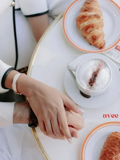A close-up of the couple holding hands over a Parisian cafe table, a simple yet powerful image of connection and shared experience.
