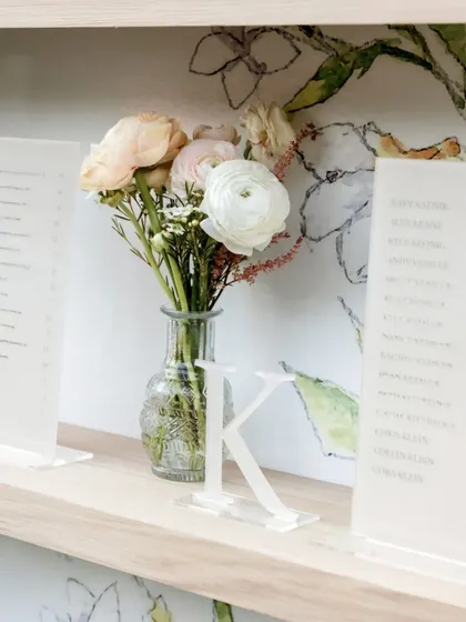 A close-up of the personalized seating chart, featuring acrylic menus and initial letters. Small bud vases with ranunculus add a delicate floral touch to the display.