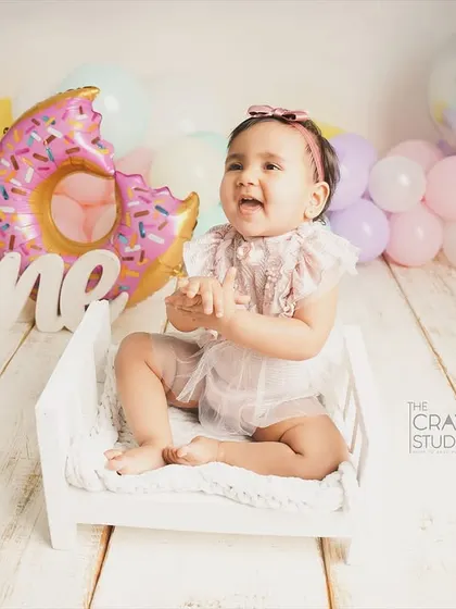 Clapping her hands with glee, this little one is having the best time at her donut-themed party, sitting on a tiny white bed.