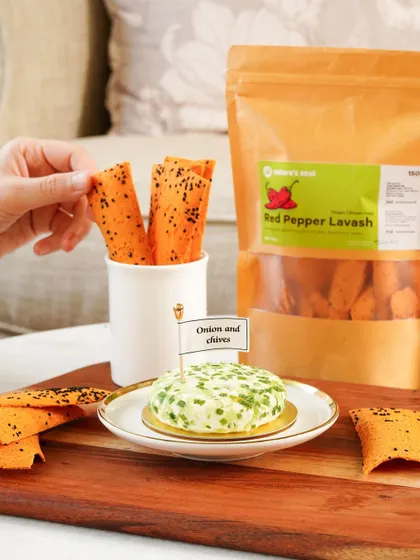 Red pepper lavash paired with an onion and chives cheese spread, styled on a wooden board for a rustic, gourmet feel.
