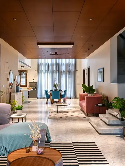 A wide-angle view of a large, open-plan living and dining area. The wooden ceiling treatment helps to define the space and adds warmth to the modern design.