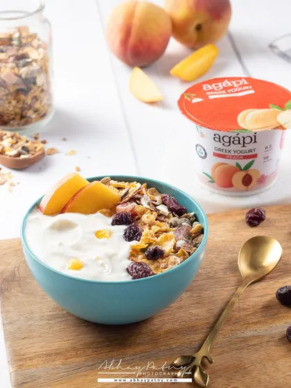 A creamy bowl of peach-flavored yogurt. The bright, airy lighting and fresh peach slices clearly communicate the flavor and the product's fresh quality.
