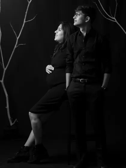 A dramatic and artistic monochrome maternity portrait. The stark branches and dark background create a powerful and moody image, highlighting the couple's connection.