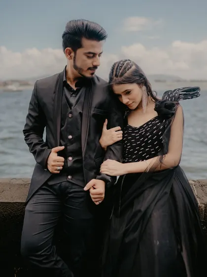 A tender moment of the bride resting her head on the groom's shoulder. Their coordinated black outfits and the sea background create a very chic and romantic image.