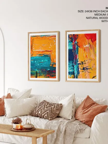 Our set of two colorful abstract paintings shown in a bright, boho-style living room. The natural wood frames with glass complement the warm tones of the room and the vibrant artwork.