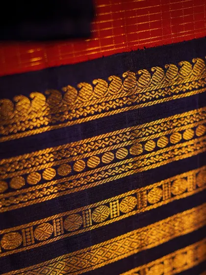 A close-up of the gold zari work on the border, featuring peacock and circle motifs, showcasing the precision of the handloom weave.