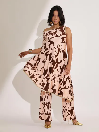 An asymmetrical printed tunic paired with matching trousers. The styling is fluid and contemporary, with gold accessories adding a touch of warmth to the brown and pink print.